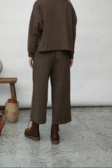 Person wearing a brown outfit standing in a room with white walls and decorative vases.